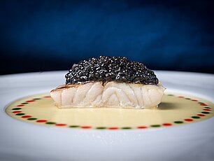 Gourmetgericht mit Fisch, belegt mit schwarzem Kaviar, auf einer cremigen Soße