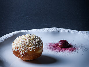 Gourmet-Donut mit geriebener Garnitur und Beerenpüree auf elegantem weißen Teller