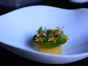 Gourmetgericht mit gelber Blütengarnitur und Kräutern in weißer Schale