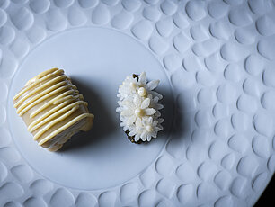 Zwei Gourmet-Desserts mit kunstvoller Dekoration auf einem strukturierten weißen Teller