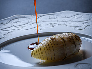 Gourmetgericht mit dünn geschnittenem Fisch und Sauce, die aus einem Löffel fließt