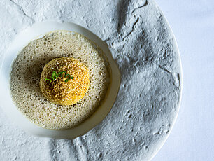 Gourmetgericht mit goldener Krokette auf cremiger Soße, garniert mit Kräutern