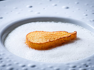 Knusprige birnenförmige Kartoffelscheibe auf cremigem weißen Schaum in strukturiertem Teller